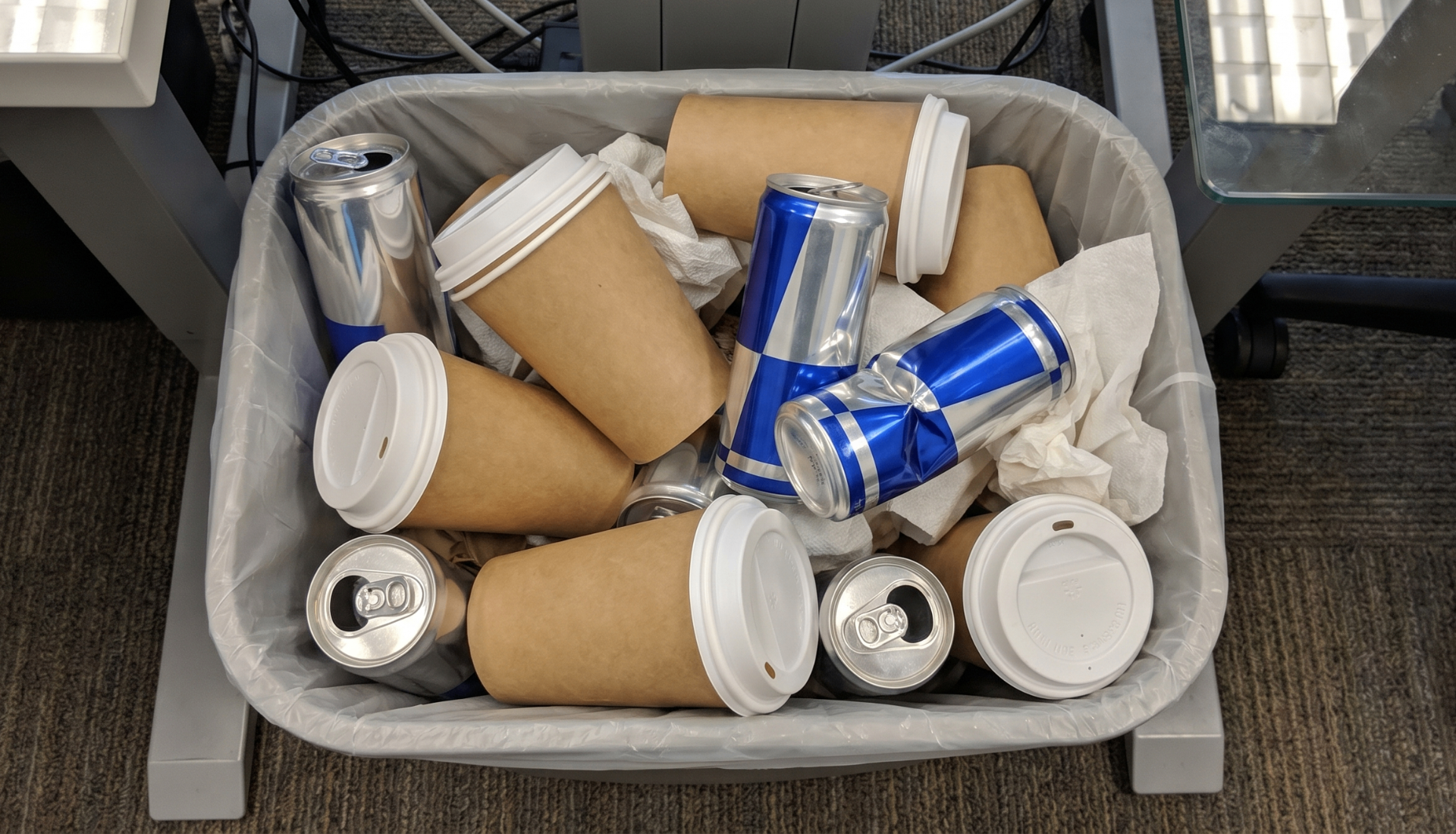 Office trash can overflowing with empty coffee cups and energy drink cans